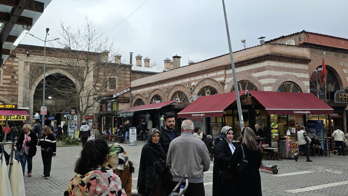 People walk past a historic stone building with arched entrances and shops, Bursa, Türkiye, March 23, 2026. (Shutterstock Photo)