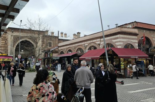 People walk past a historic stone building with arched entrances and shops, Bursa, Türkiye, March 23, 2026. (Shutterstock Photo)
