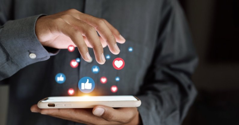 A close-up of a hand using a smartphone with social media icons floating above the screen. (Shutterstock Photo)