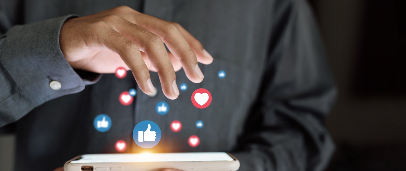 A close-up of a hand using a smartphone with social media icons floating above the screen. (Shutterstock Photo)