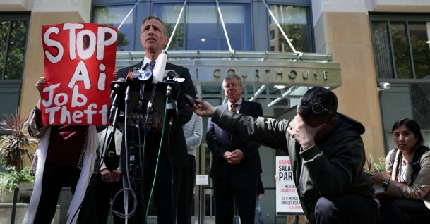A demonstrator holds a placard as attorney William Savitt, representing OpenAI, speaks to the press outside the federal courthouse, as the trial in Elon Musk's lawsuit over OpenAI's for-profit conversion continues, in Oakland, California, U.S., May 18, 2026. (Reuters Photo)