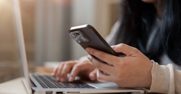 A woman uses her smartphone while working on her laptop. (Shutterstock Photo)