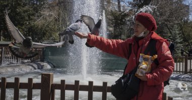 A visitor feeds pigeons in a park on a sunny day, Ankara, Türkiye, March 31, 2023. (Getty Images Photo)