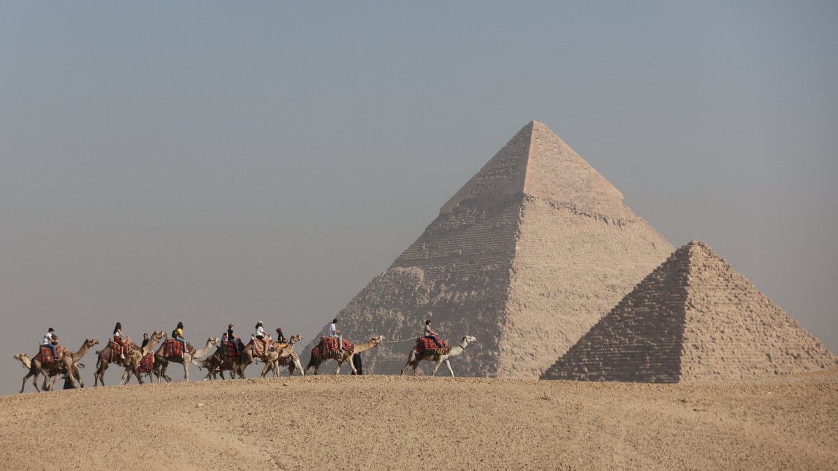 Tourists ride camels in front of the Great Pyramids plateau, Giza, Egypt, Dec. 11, 2022. (Reuters Photo)