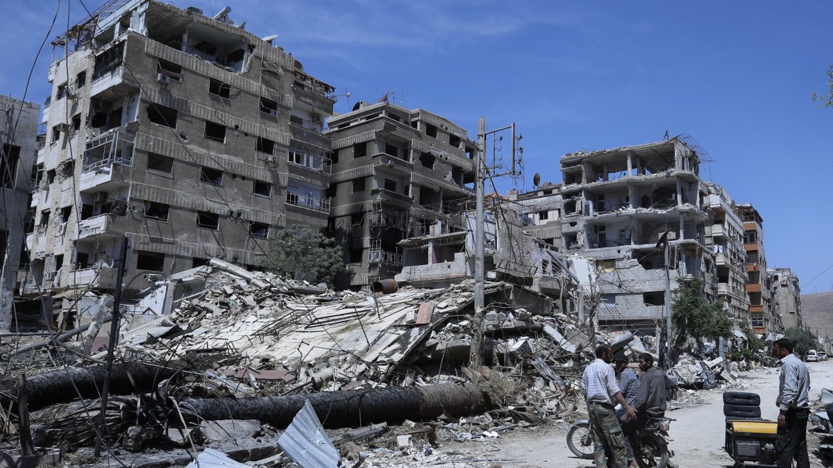 People stand in front of damaged buildings, in the town of Douma, the site of a suspected chemical weapons attack, near Damascus, Syria, April 16, 2018. (AP File Photo)