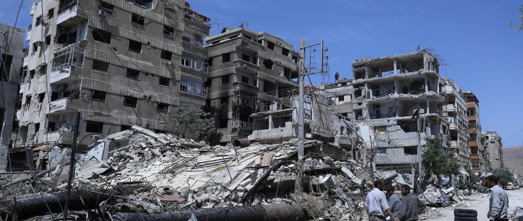 People stand in front of damaged buildings, in the town of Douma, the site of a suspected chemical weapons attack, near Damascus, Syria, April 16, 2018. (AP File Photo)