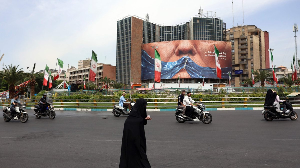 An Iranian woman crosses the road next to a political billboard featuring U.S. President Donald Trump and the Strait of Hormuz erected on a building in Valiasr Square, in Tehran, May 28, 2026. (AFP Photo)