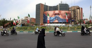 An Iranian woman crosses the road next to a political billboard featuring U.S. President Donald Trump and the Strait of Hormuz erected on a building in Valiasr Square, in Tehran, May 28, 2026. (AFP Photo)