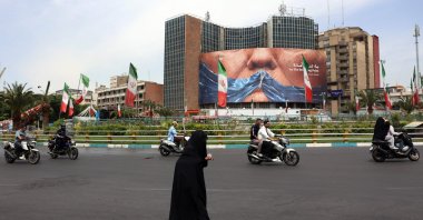 An Iranian woman crosses the road next to a political billboard featuring U.S. President Donald Trump and the Strait of Hormuz erected on a building in Valiasr Square, in Tehran, May 28, 2026. (AFP Photo)