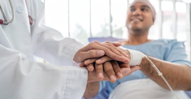 A male cancer patient in a wheelchair receives IV therapy while a doctor provides support. (Shutterstock Photo)