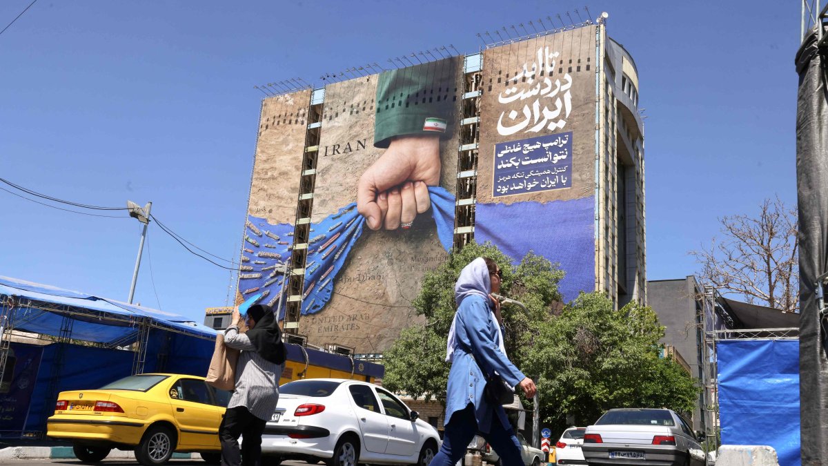People cross a street near a billboard on the facade of a building depicting the Strait of Hormuz with a caption in Persian reading "Forever in Iran’s Hand," Vanak Square, Tehran, Iran, May 25, 2026. (AFP Photo)