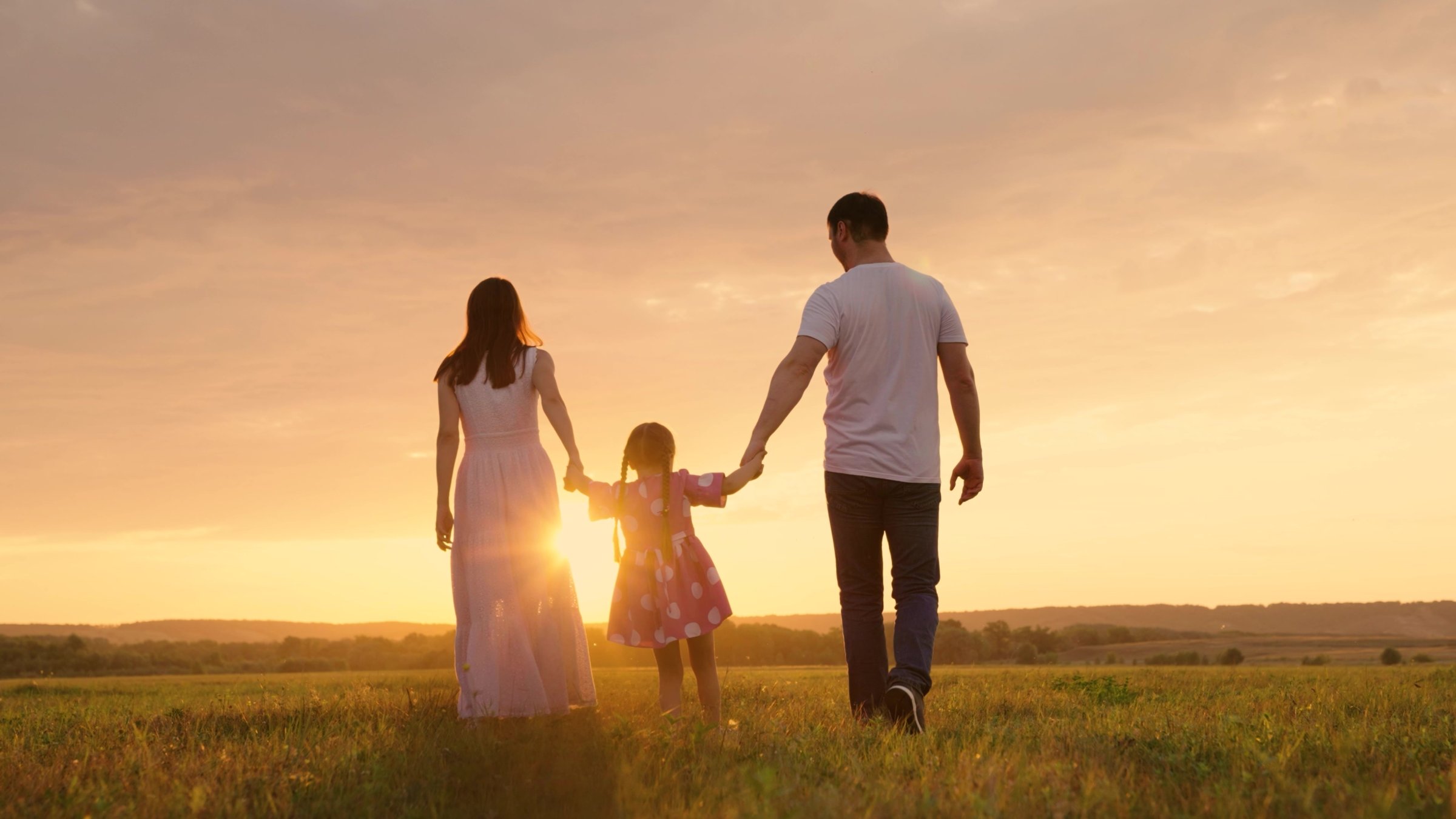 Parents and daughter run at sunset as the child holds their hands and jumps. (Shutterstock Photo)