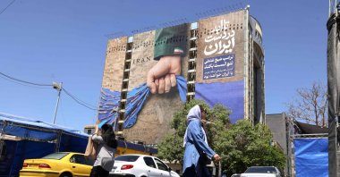 People cross a street near a billboard on the facade of a building depicting the Strait of Hormuz with a caption in Persian reading "Forever in Iran’s Hand," Vanak Square, Tehran, Iran, May 25, 2026. (AFP Photo)