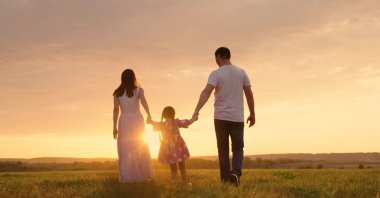 Parents and daughter run at sunset as the child holds their hands and jumps. (Shutterstock Photo)