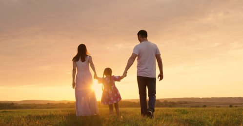 Parents and daughter run at sunset as the child holds their hands and jumps. (Shutterstock Photo)