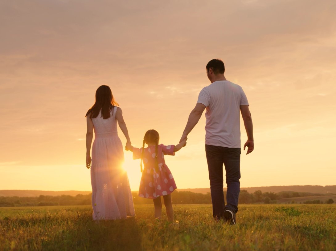 Parents and daughter run at sunset as the child holds their hands and jumps. (Shutterstock Photo)