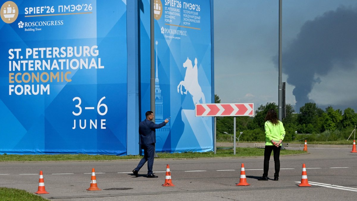 People are seen in front of banners with branding for the St. Petersburg International Economic Forum (SPIEF) as black smoke rises in the distance, St. Petersburg, Russia, June 3, 2026. (AFP Photo)
