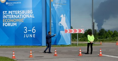 People are seen in front of banners with branding for the St. Petersburg International Economic Forum (SPIEF) as black smoke rises in the distance, St. Petersburg, Russia, June 3, 2026. (AFP Photo)
