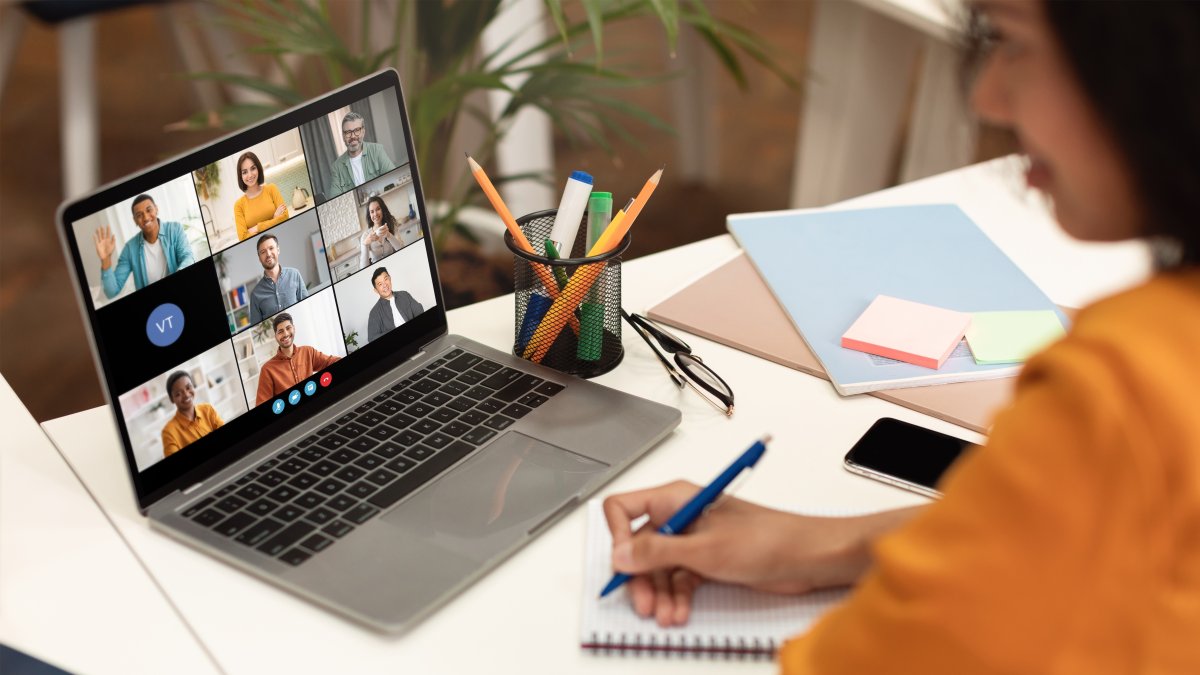 A woman sits at a desk with a laptop open, displaying a video conference meeting with several participants. (Shutterstock Photo)