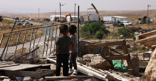 Palestinian children watch as new prefabricated Jewish outpost homes are secured into place along a road that leads toward the Palestinian village of Umm al-Khair, in Israeli-occupied West Bank, Palestine, May 20, 2026. (AFP Photo)