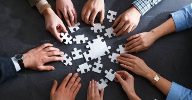 In this undated stock photo, group of businesspeople put puzzle pieces together on a table. (Shutterstock Photo)