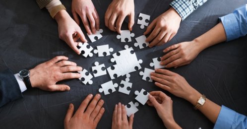 In this undated stock photo, group of businesspeople put puzzle pieces together on a table. (Shutterstock Photo)