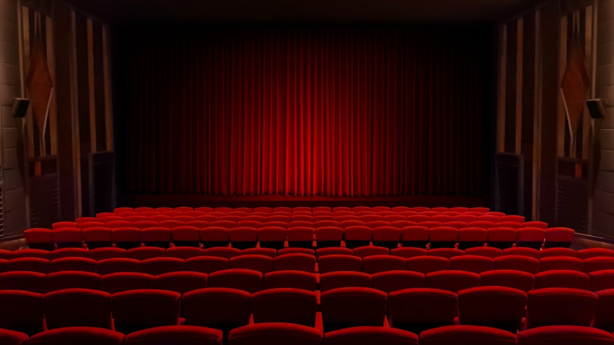 Empty theater seats facing red velvet stage curtain. (Shutterstock Photo)
