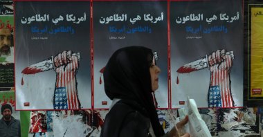A woman passes by wall-mounted political posters depicting a hand decorated in the colors of the U.S. flag holding a dagger that symbolizes Israel and reading "America is a plague, and the plague is America," Beirut, Lebanon, June 9, 2026. (EPA Photo)