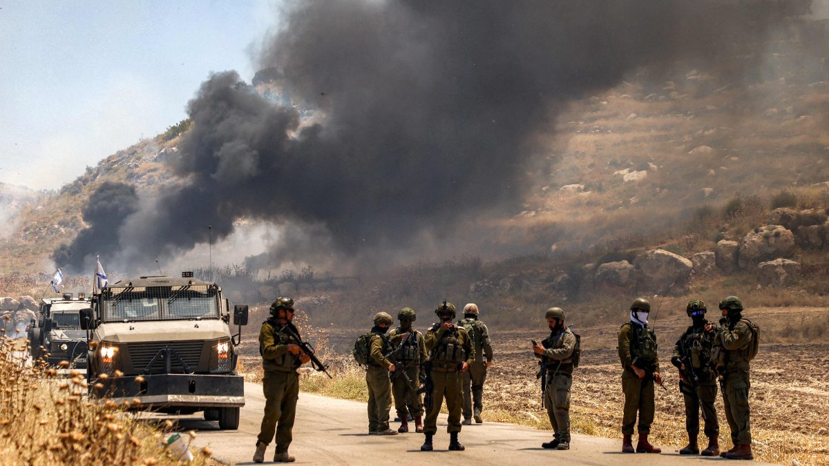 Israeli security forces stand guard along a road while behind smoke billows from an area set ablaze by Israeli settlers in the Palestinian village of Idna, west of Hebron in the occupied West Bank, June 5, 2026. (AFP Photo)