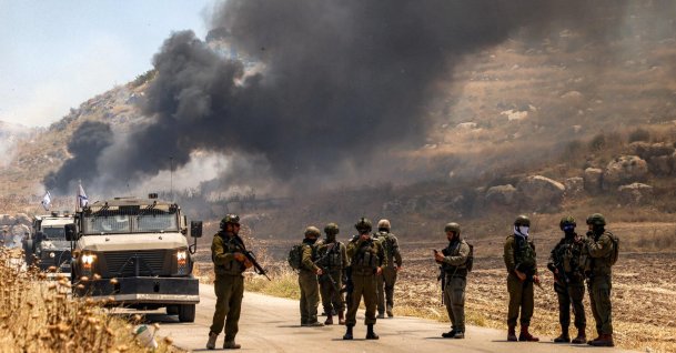 Israeli security forces stand guard along a road while behind smoke billows from an area set ablaze by Israeli settlers in the Palestinian village of Idna, west of Hebron in the occupied West Bank, June 5, 2026. (AFP Photo)