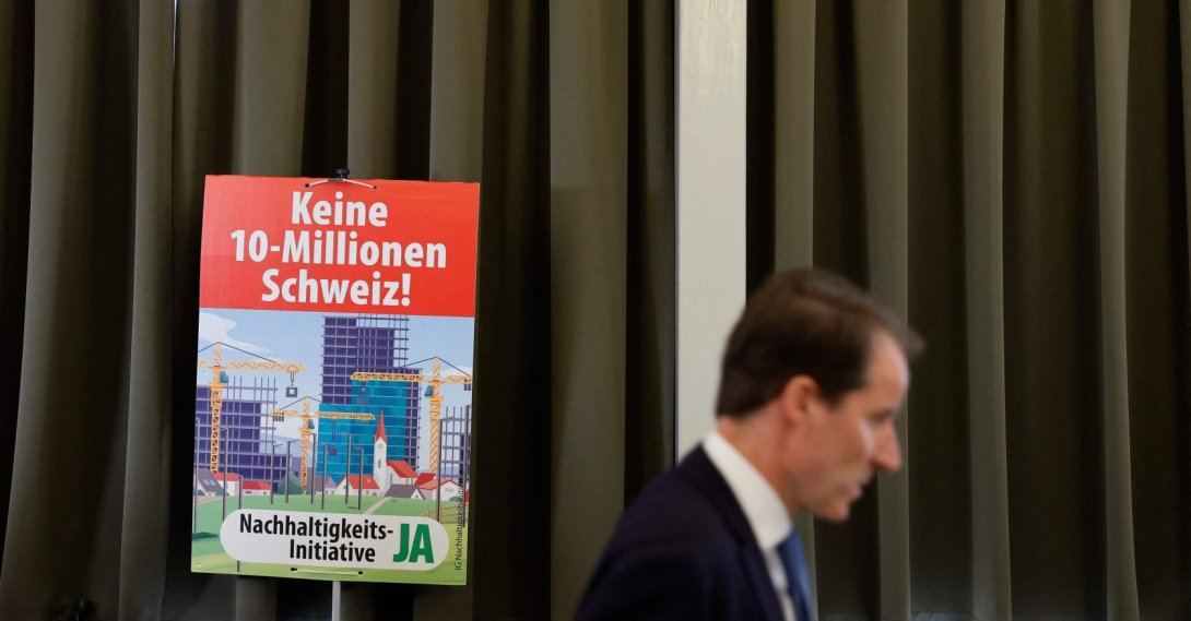 A member of the Swiss People's Party (SVP) walks past an election placard reading "Not a 10-million Switzerland" in Aarberg, Switzerland, June 14, 2026. (AFP Photo)