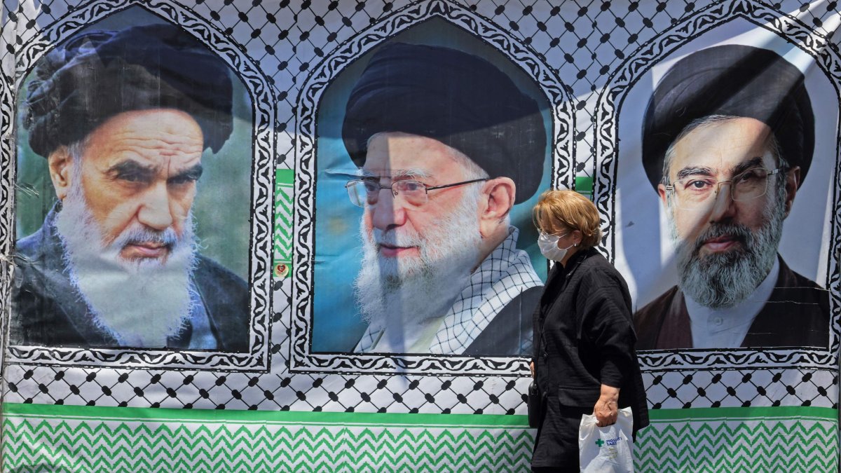 A woman walks past a banner bearing the images of the late Ayatollah Ruhollah Khomeini (L), the late supreme leader Ali Khamenei, and his son, the current supreme leader Mojtaba Khamenei (R), Tehran, Iran, June 10, 2026. (AFP Photo)