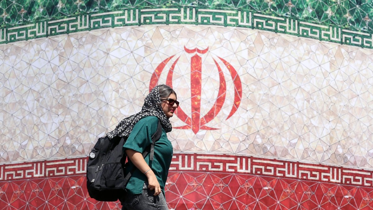 An Iranian woman walks past a billboard featuring Iran's national flag at Enqelab Square in Tehran, Iran, June 14, 2026. (EPA Photo)