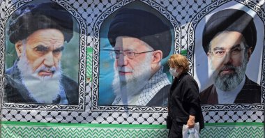 A woman walks past a banner bearing the images of the late Ayatollah Ruhollah Khomeini (L), the late supreme leader Ali Khamenei, and his son, the current supreme leader Mojtaba Khamenei (R), Tehran, Iran, June 10, 2026. (AFP Photo)