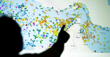 A photo illustration shows a person in front of a large screen displaying vessel movements in the Strait of Hormuz on a ship-tracking website, May 4, 2026. (AFP Photo)