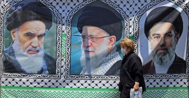 A woman walks past a banner bearing the images of the late Ayatollah Ruhollah Khomeini (L), the late supreme leader Ali Khamenei, and his son, the current supreme leader Mojtaba Khamenei (R), Tehran, Iran, June 10, 2026. (AFP Photo)
