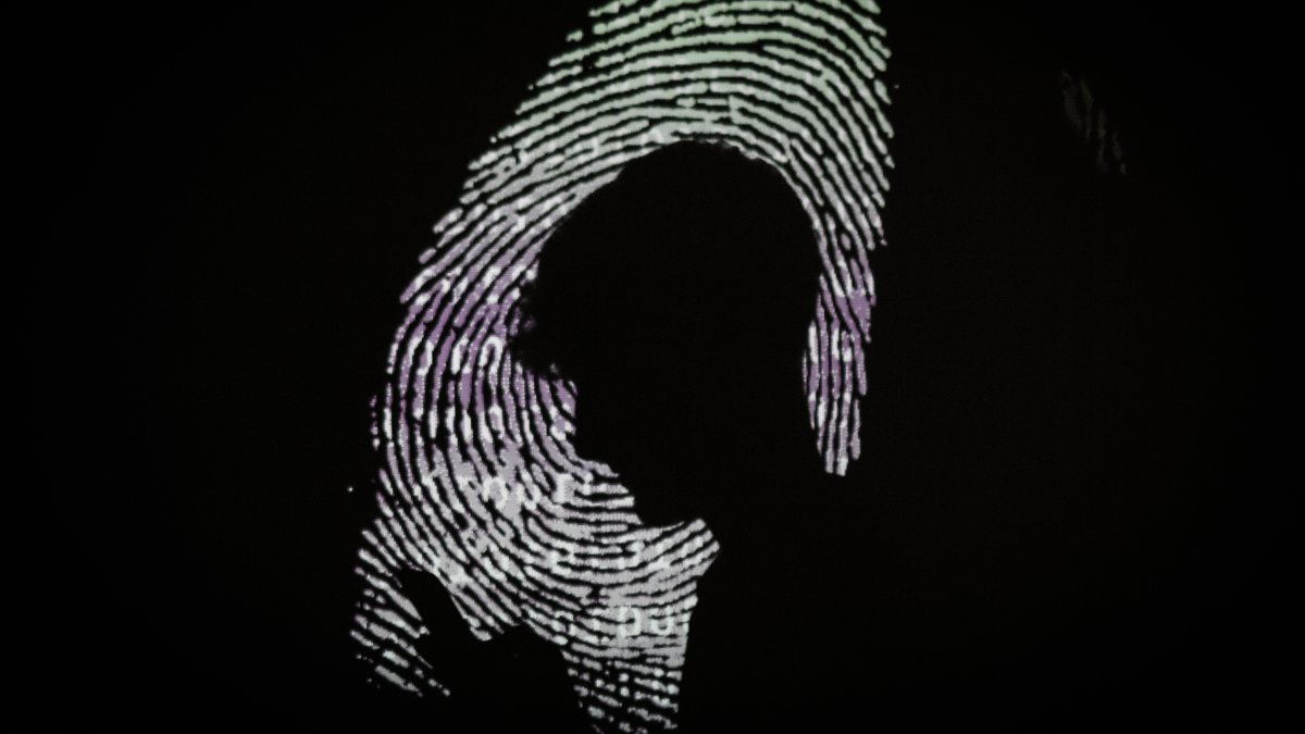 A man using a mobile phone in the light of a projection of a thumbprint, London, England, Aug. 9, 2017. (Getty Images Photo)