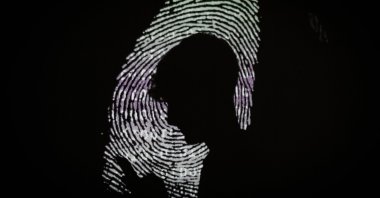 A man using a mobile phone in the light of a projection of a thumbprint, London, England, Aug. 9, 2017. (Getty Images Photo)