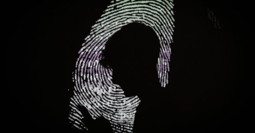 A man using a mobile phone in the light of a projection of a thumbprint, London, England, Aug. 9, 2017. (Getty Images Photo)