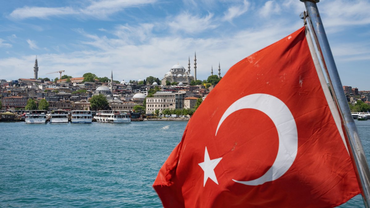 A Turkish national flag waves behind a tour boat sailing along the turquoise waters of the Bosporus, with the city's iconic skyline in the background, Istanbul, Türkiye, June 4, 2026. (Getty Images Photo)