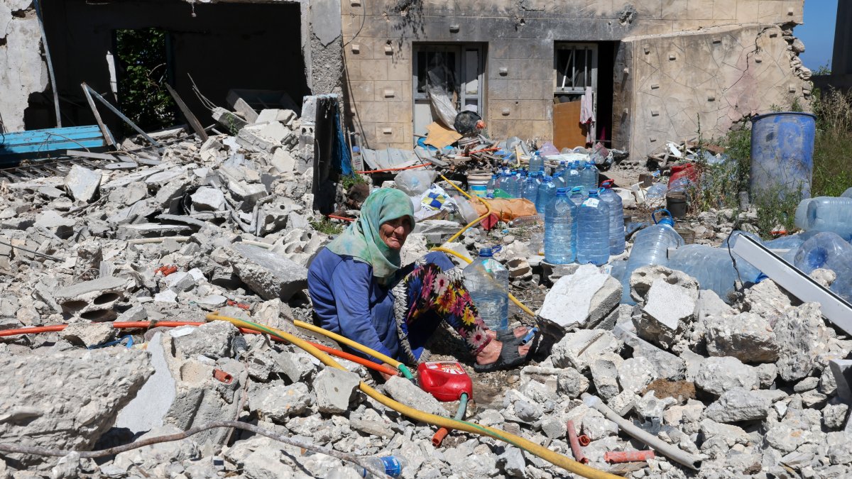 Khadija Amara, an elderly woman, fills a jerrycan with water as she sits amid the rubble of her house, damaged by an Israeli strike, in the village of Qlaileh, southern Lebanon, June 19, 2026. (EPA Photo)