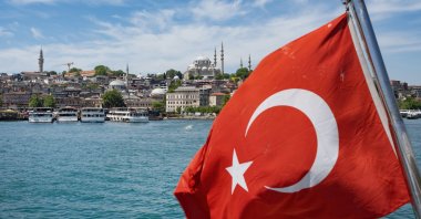 A Turkish national flag waves behind a tour boat sailing along the turquoise waters of the Bosporus, with the city's iconic skyline in the background, Istanbul, Türkiye, June 4, 2026. (Getty Images Photo)
