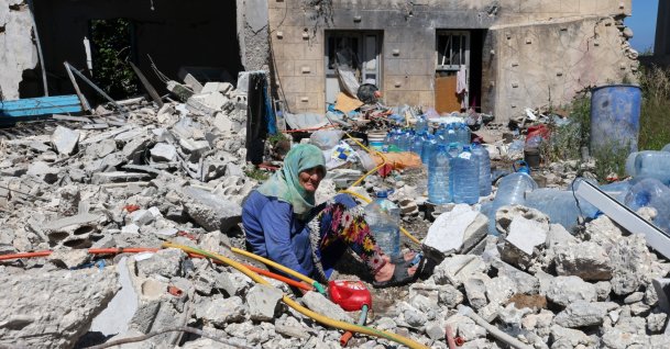 Khadija Amara, an elderly woman, fills a jerrycan with water as she sits amid the rubble of her house, damaged by an Israeli strike, in the village of Qlaileh, southern Lebanon, June 19, 2026. (EPA Photo)