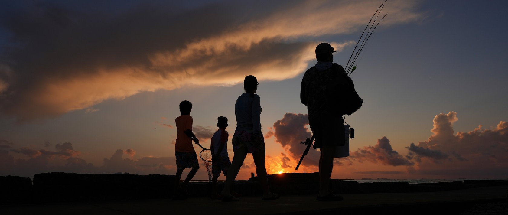 A family prepares to fish along a jetty at sunrise in Port Aransas, Texas, U.S., Aug. 10, 2025. (AP Photo)