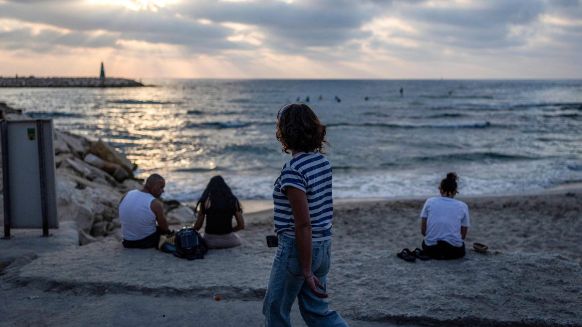 A woman walks past people sitting along a beach in Tel Aviv, Israel, June 8, 2026. (AFP Photo)
