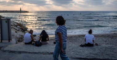 A woman walks past people sitting along a beach in Tel Aviv, Israel, June 8, 2026. (AFP Photo)