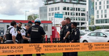 Damaged windows can be seen in the distance as police gather near the scene of a shooting in Montreal, June 22, 2026. (AFP Photo)