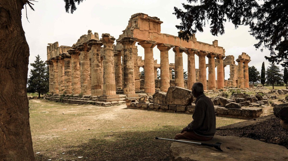 A man sits in the shade in front of the Temple of Zeus at the archaeological site of Cyrene, near the town of Shahat, Libya, May 18, 2026. (AFP Photo)