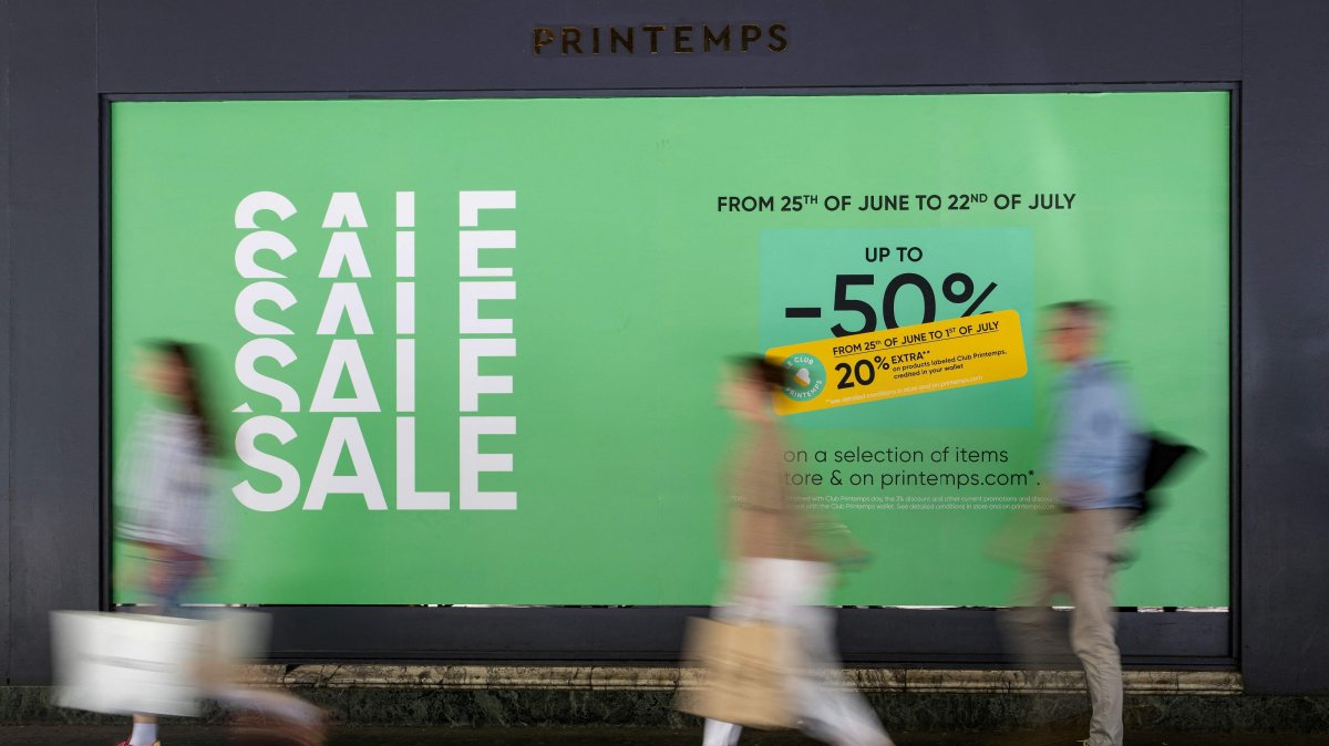 People walk past a board displayed on the shop window of a department store advertising discounts up to 50% on the first day of the French summer sales in Paris, June 25, 2025. (AFP Photo)