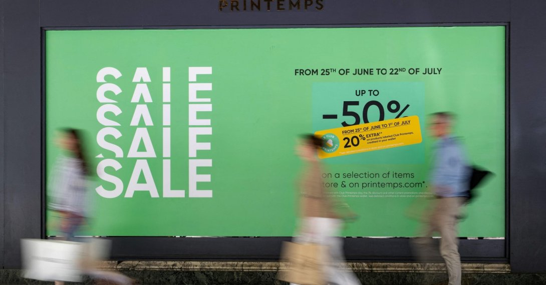 People walk past a board displayed on the shop window of a department store advertising discounts up to 50% on the first day of the French summer sales in Paris, June 25, 2025. (AFP Photo)